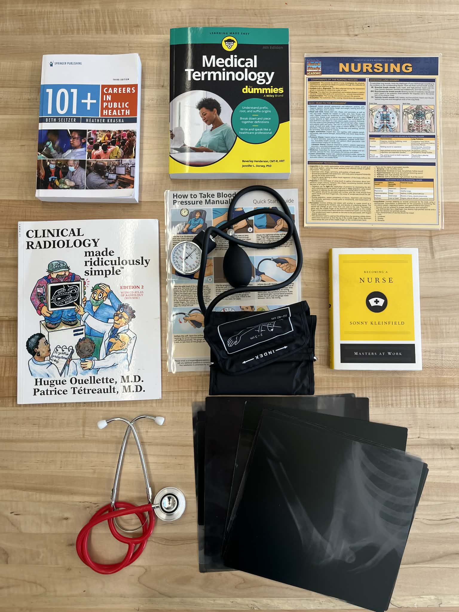 Medical study essentials on a wooden table: books on public health, medical terminology, radiology, and nursing, with a stethoscope, blood pressure cuff, and X-ray films.