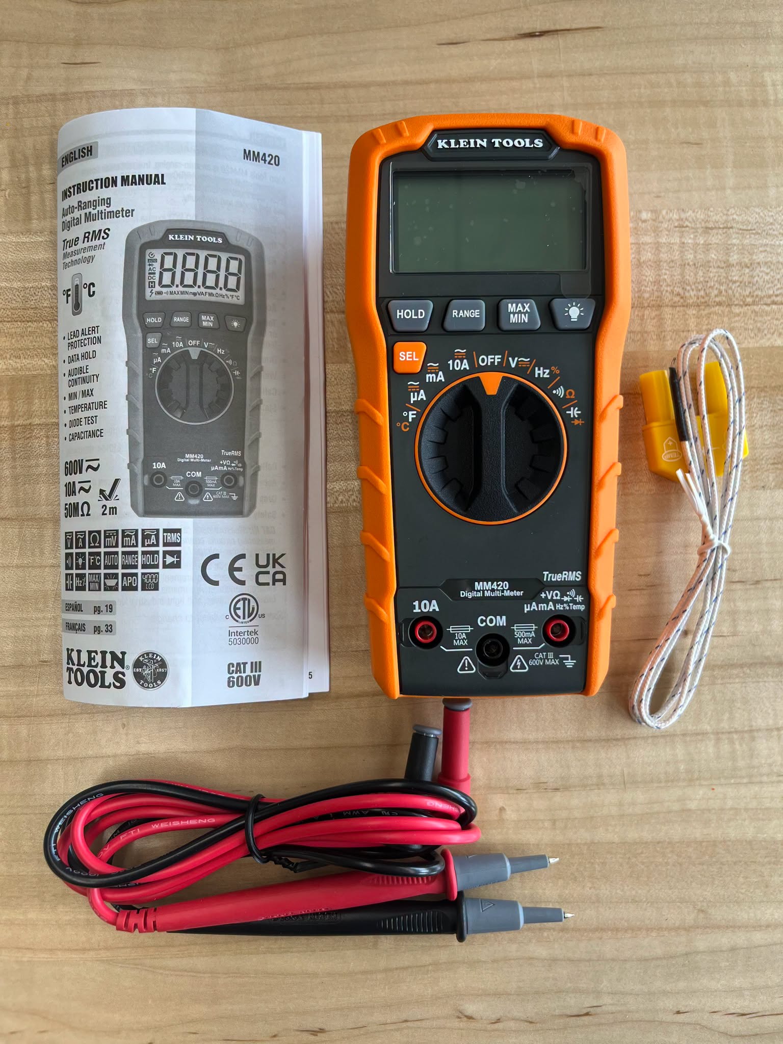 A digital multimeter displayed alongside a battery and connecting wires, used for measuring electrical values.<br />
