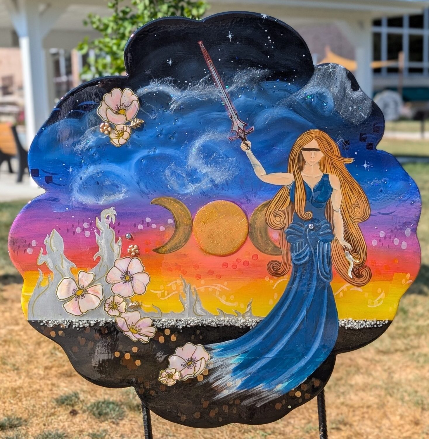Poppy cut-out with a painting of a fantasy world with moons, flowers, a heroine, and sparkles