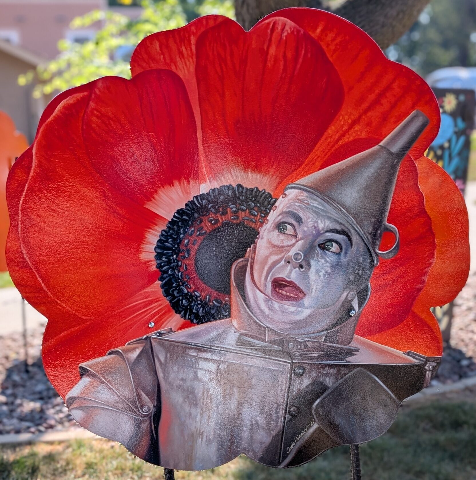 poppy cut-out painted as a hyper-realistic red poppy with a hyper-realistic tin man in front