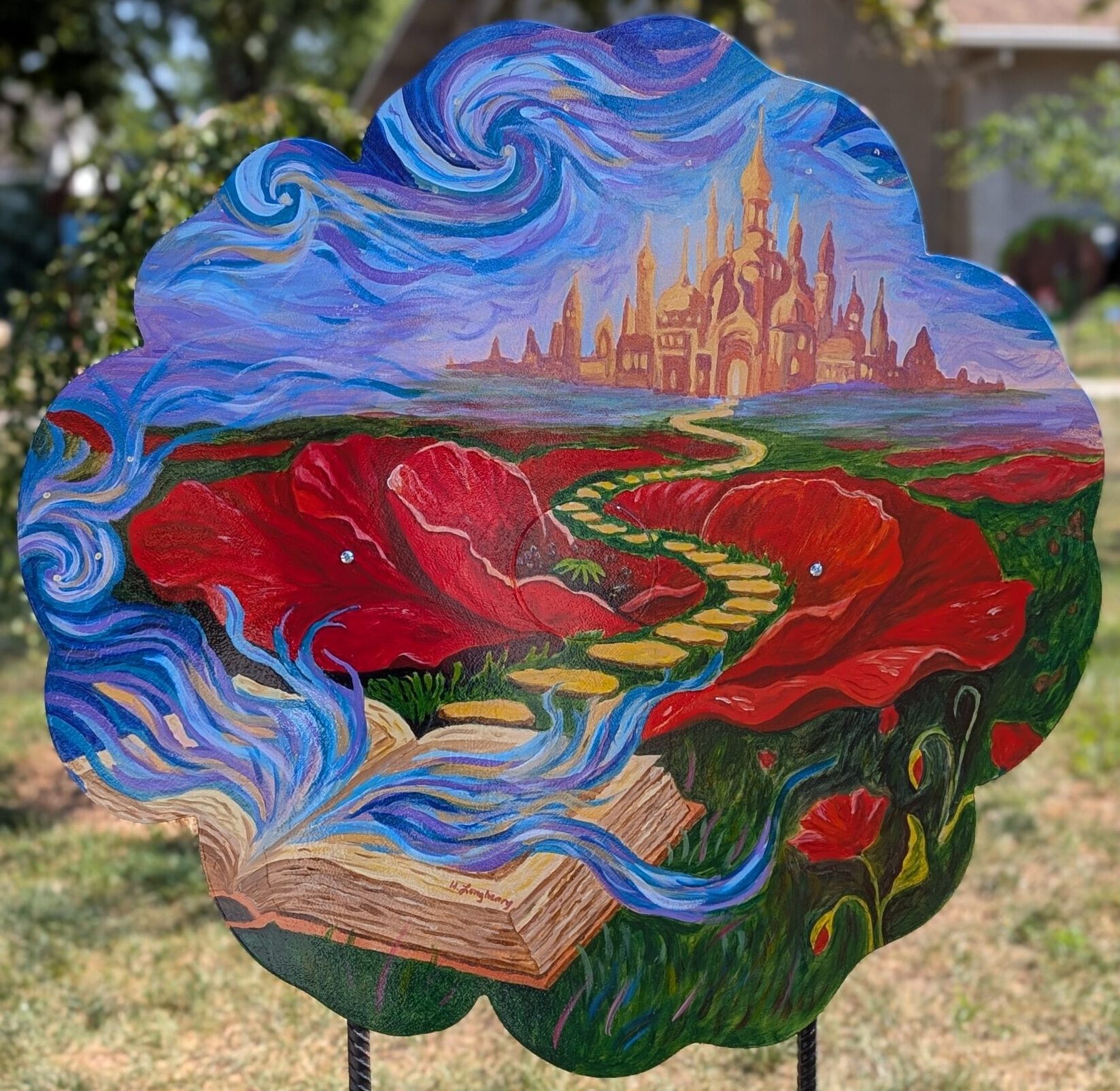Poppy cut-out painted with a scene of an open book, a yellow brick road through large poppies leading to a magical city in the distance