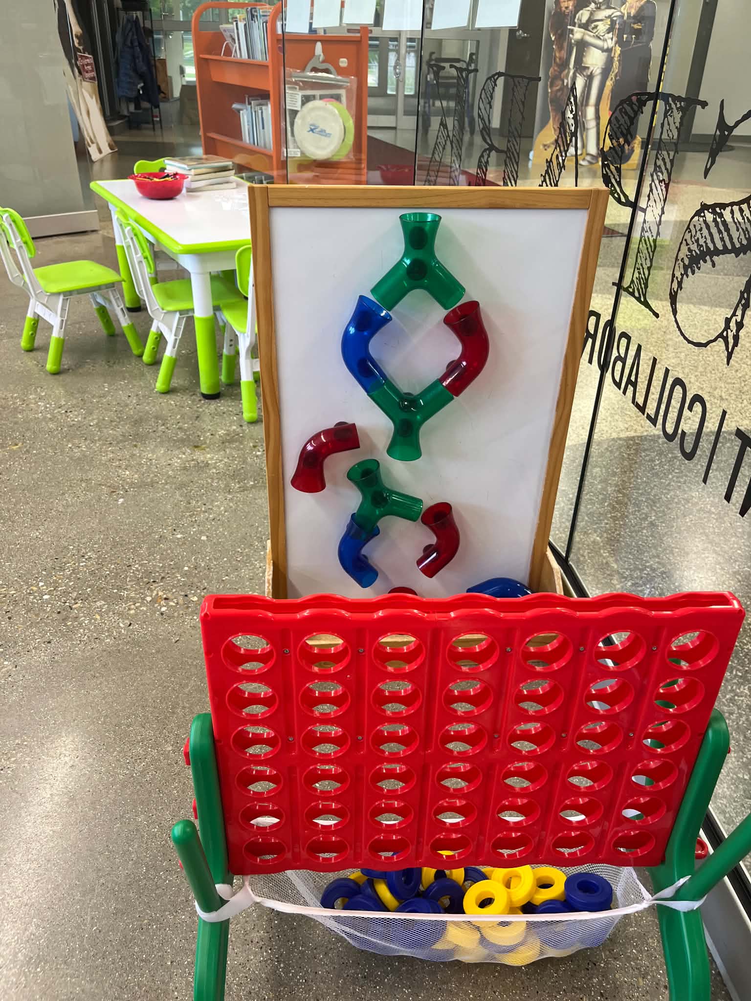 Colorful play area with a Connect Four game, interlocking plastic shapes, and a table with colorful chairs, featuring a bowl of toys.<br />
